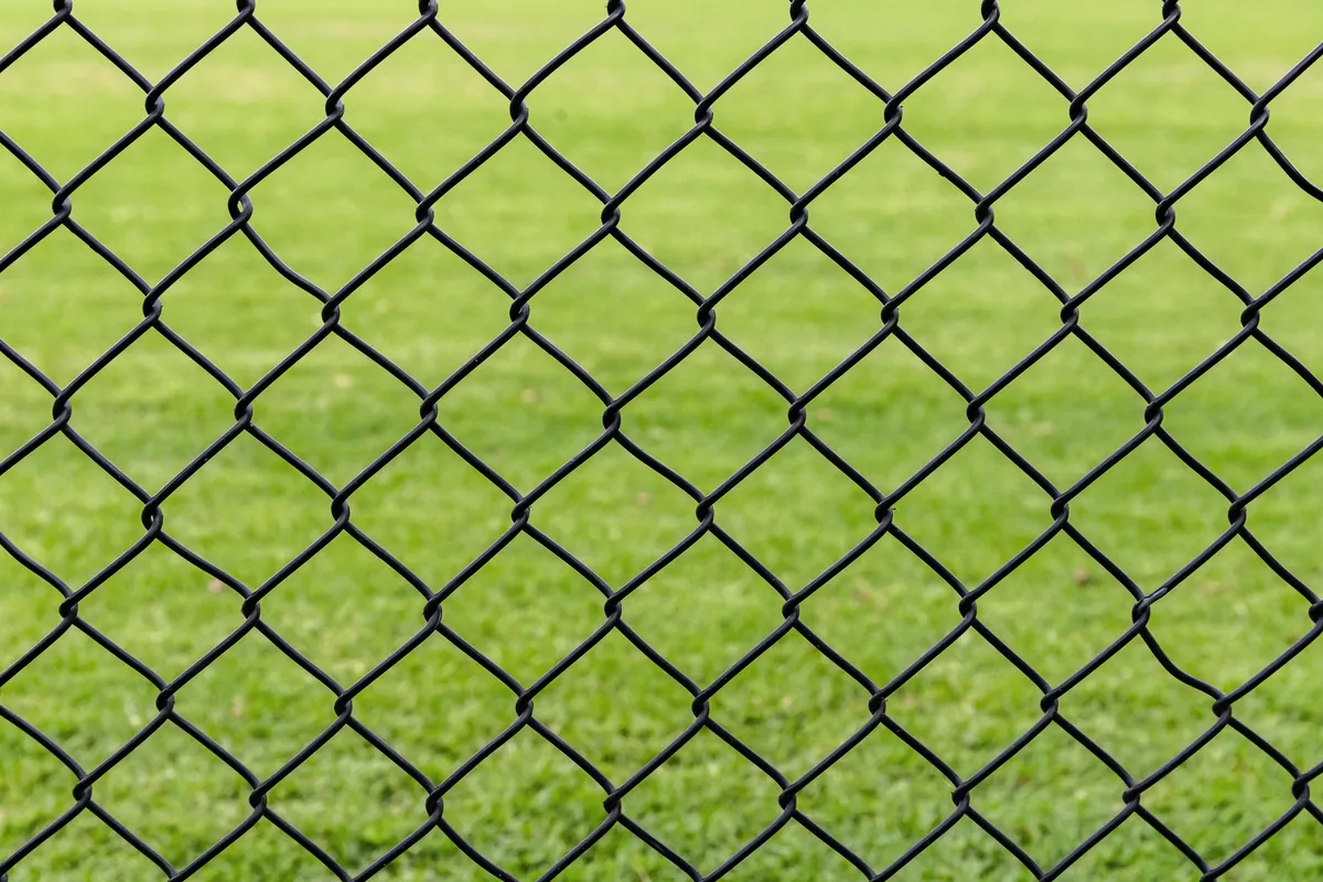 Black vinyl-coated chain link fence in front of a green field